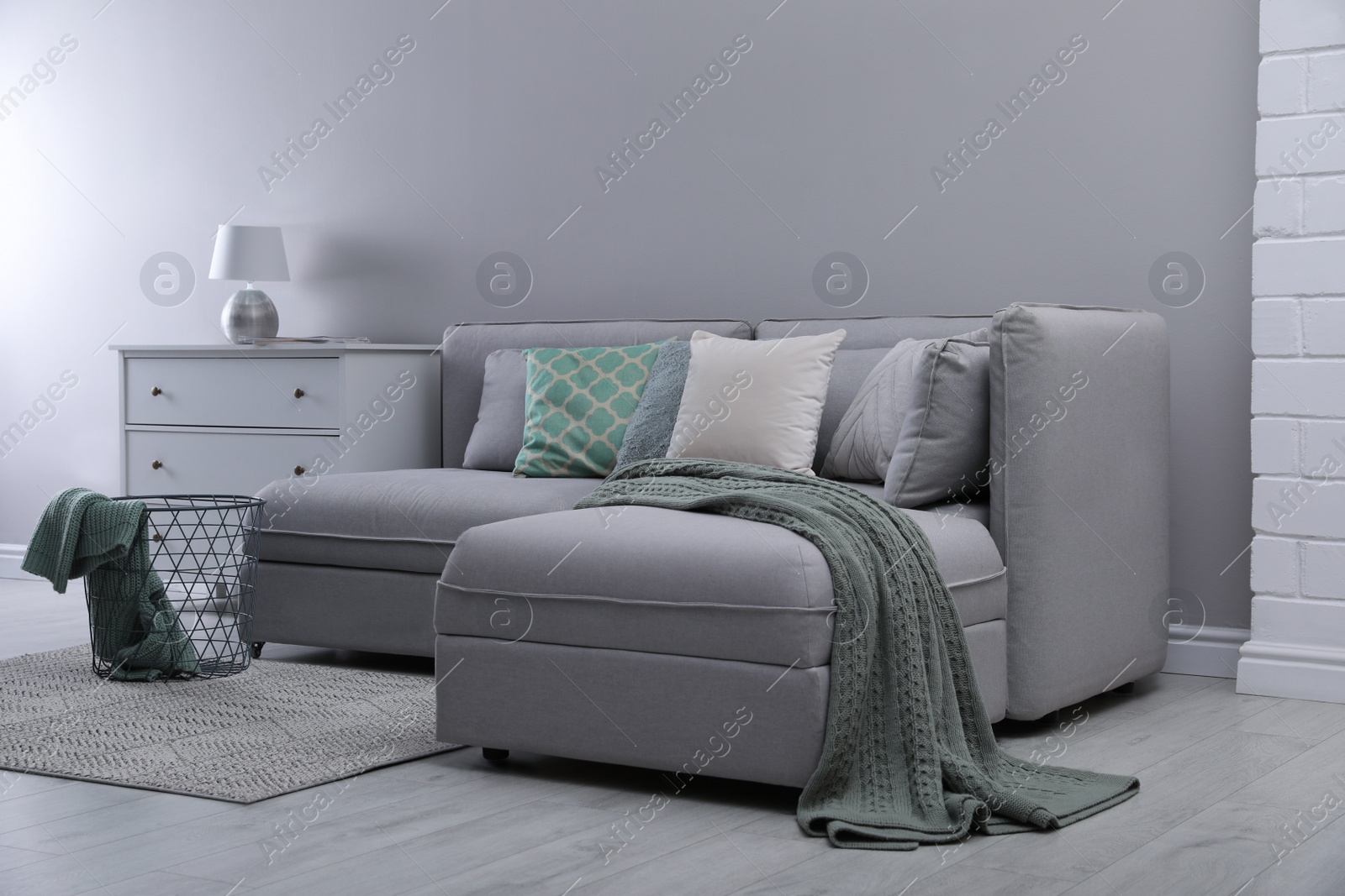 Photo of Large grey sofa and chest of drawers near light wall in room. Interior design