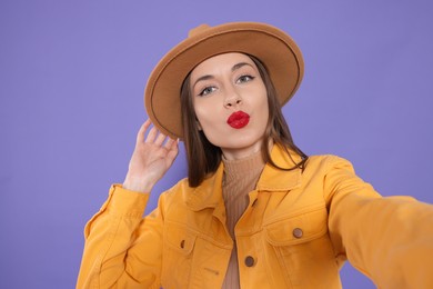 Photo of Beautiful young woman blowing kiss while taking selfie on purple background