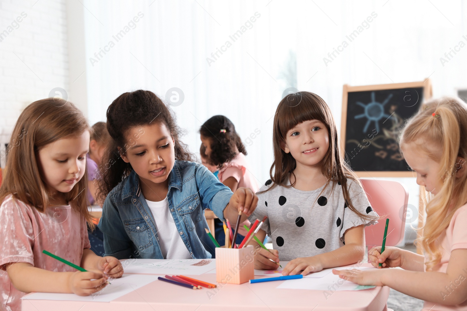 Photo of Adorable children drawing together at table indoors. Kindergarten playtime activities