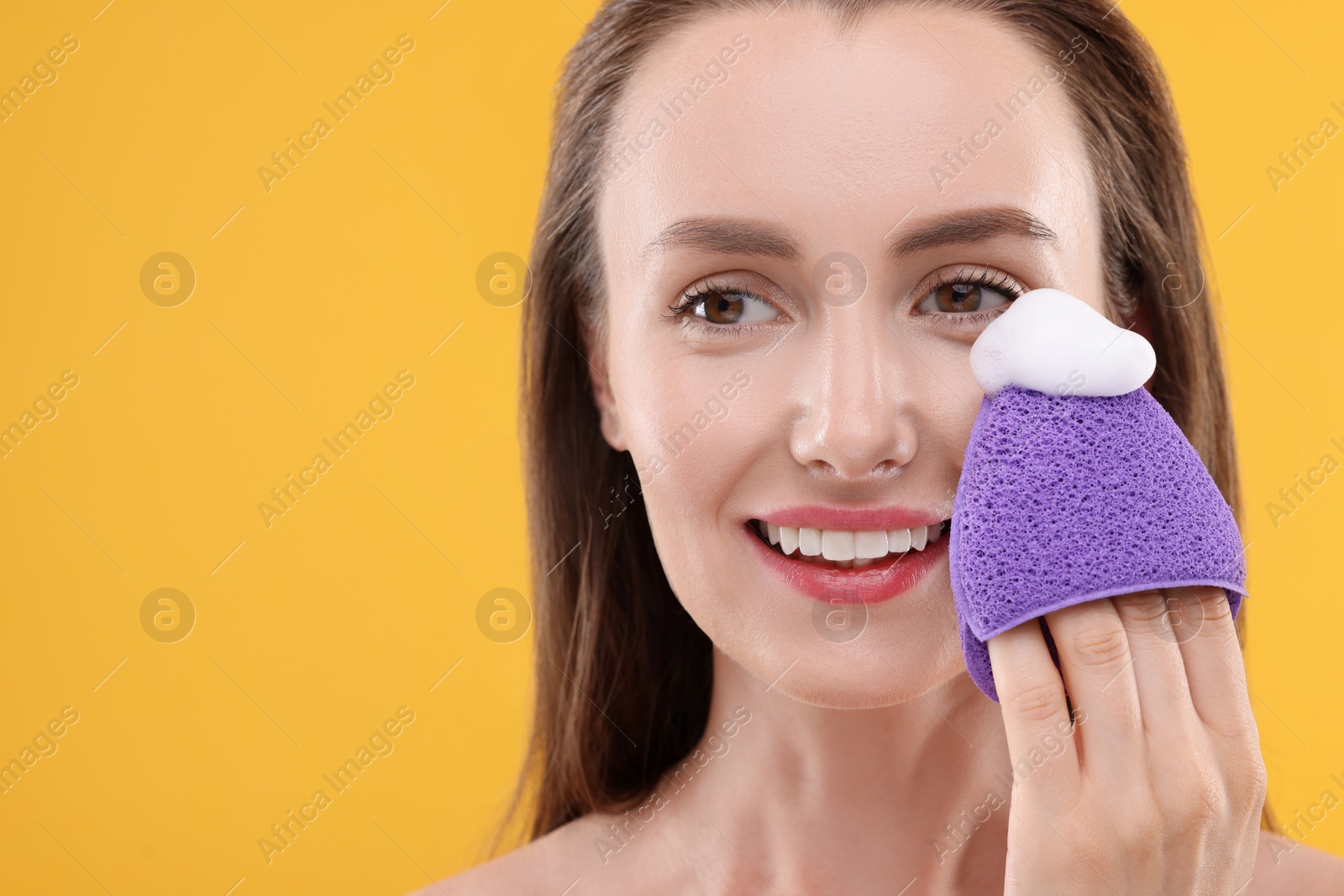 Photo of Happy young woman washing her face with sponge on orange background. Space for text