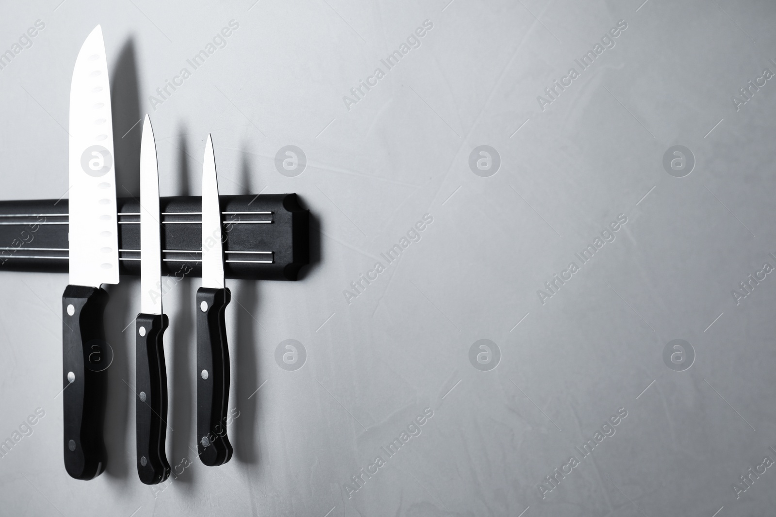 Photo of Magnetic holder with set of knives on grey stone background. Space for text