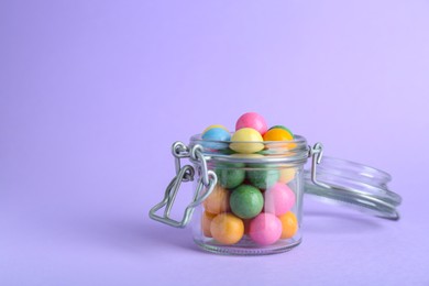 Photo of Jar with many bright gumballs on lilac background. Space for text