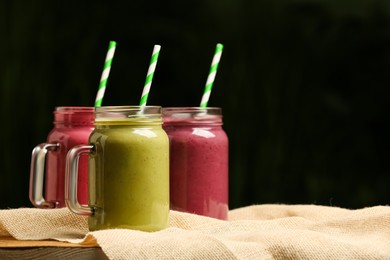 Photo of Different delicious smoothies in mason jars on table against dark background, space for text