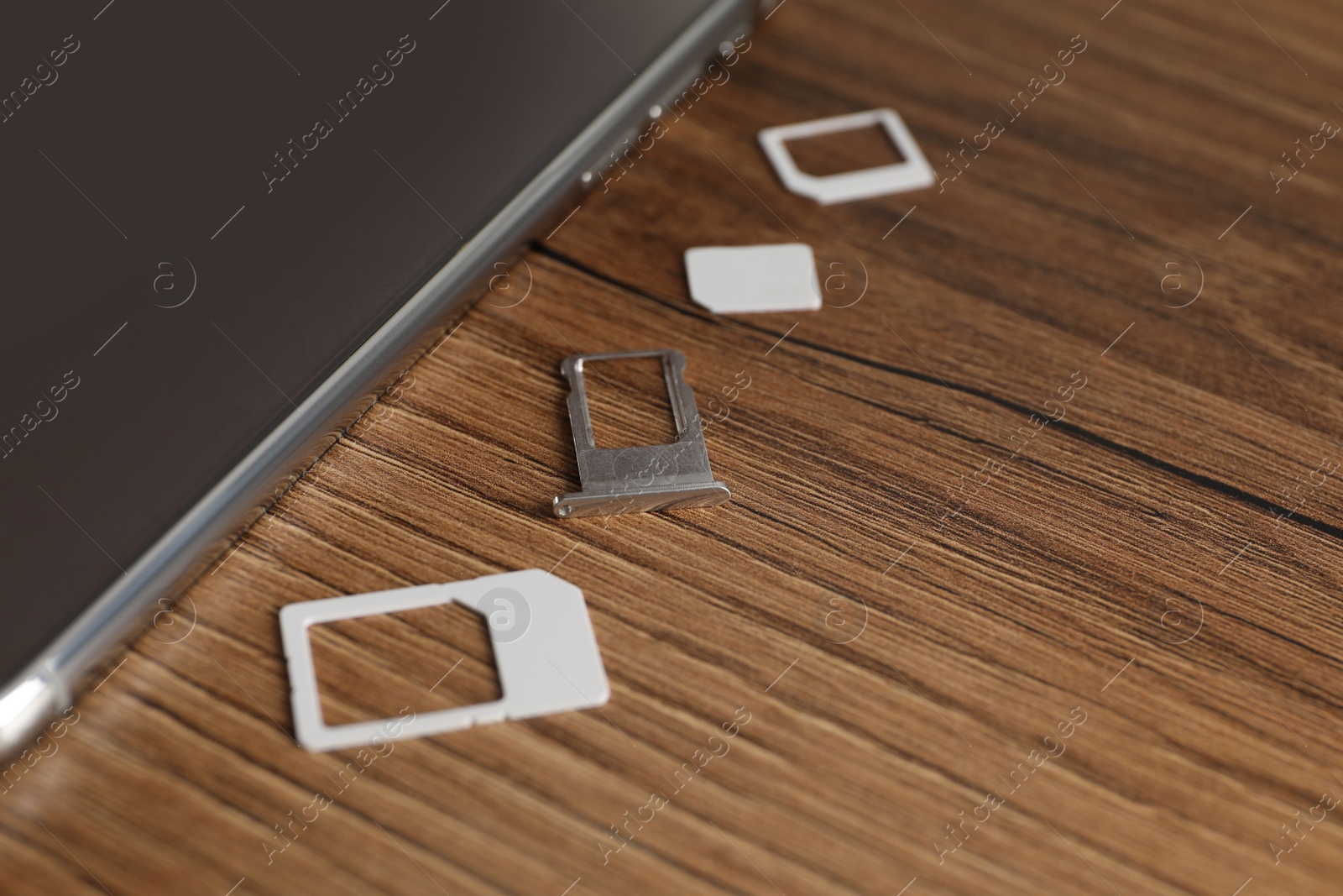 Photo of Mobile phone, SIM card and tray on wooden table, closeup