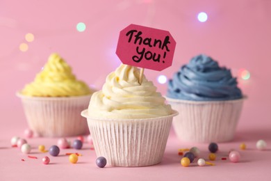 Photo of Tasty cupcakes and note with phrase Thank You on pale pink background