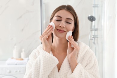 Photo of Young woman with cotton pads cleaning her face in bathroom