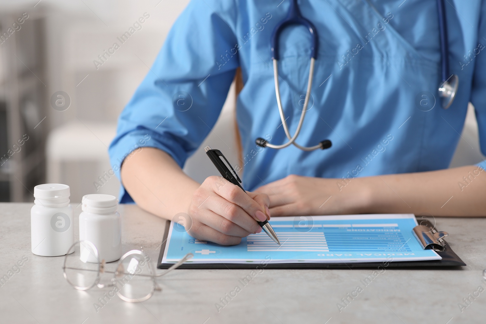 Photo of Doctor filling patient's medical card at table in clinic, closeup