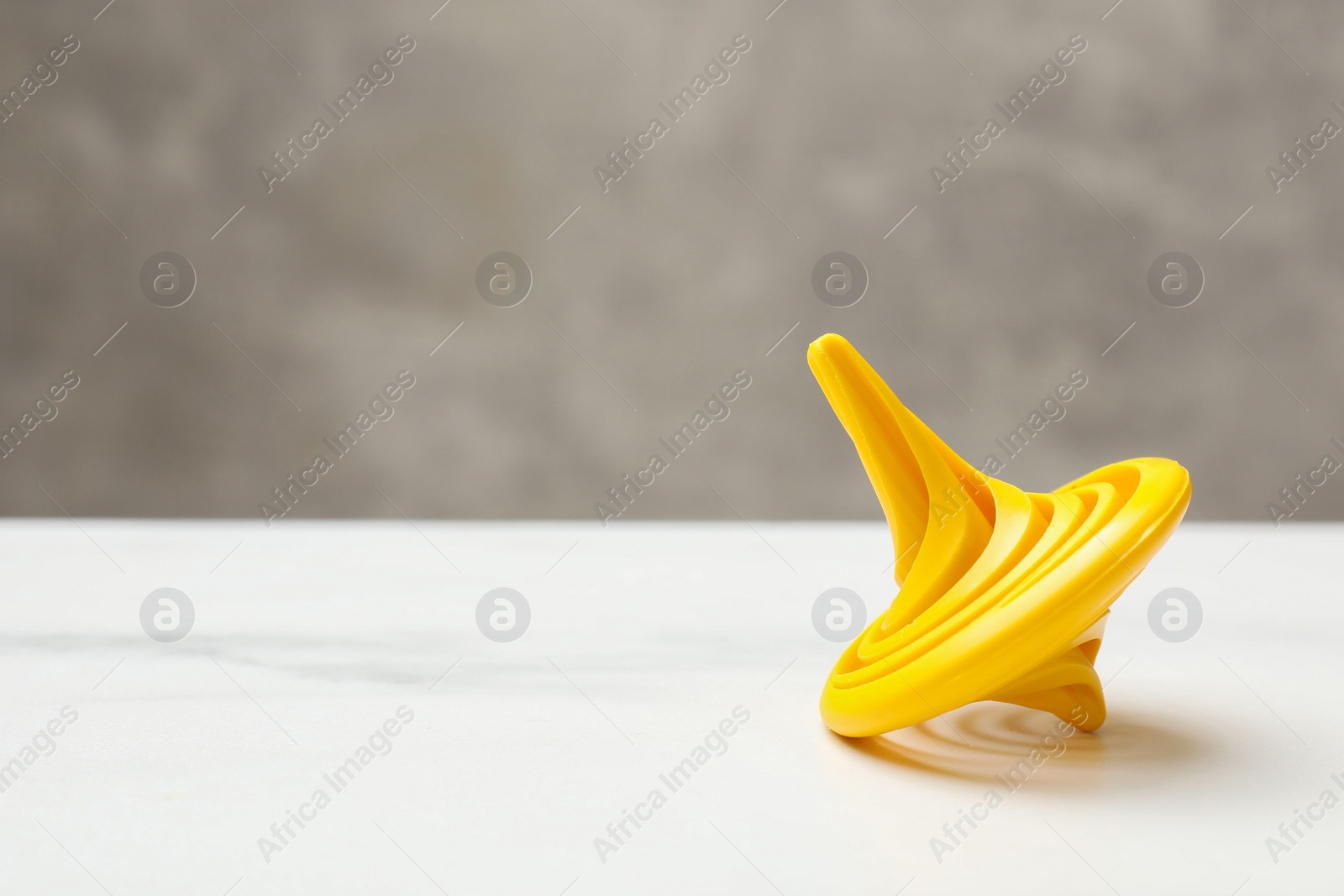 Photo of One yellow spinning top on white table, closeup. Space for text