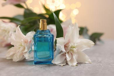 Bottle of perfume and beautiful lily flowers on table against beige background with blurred lights, closeup