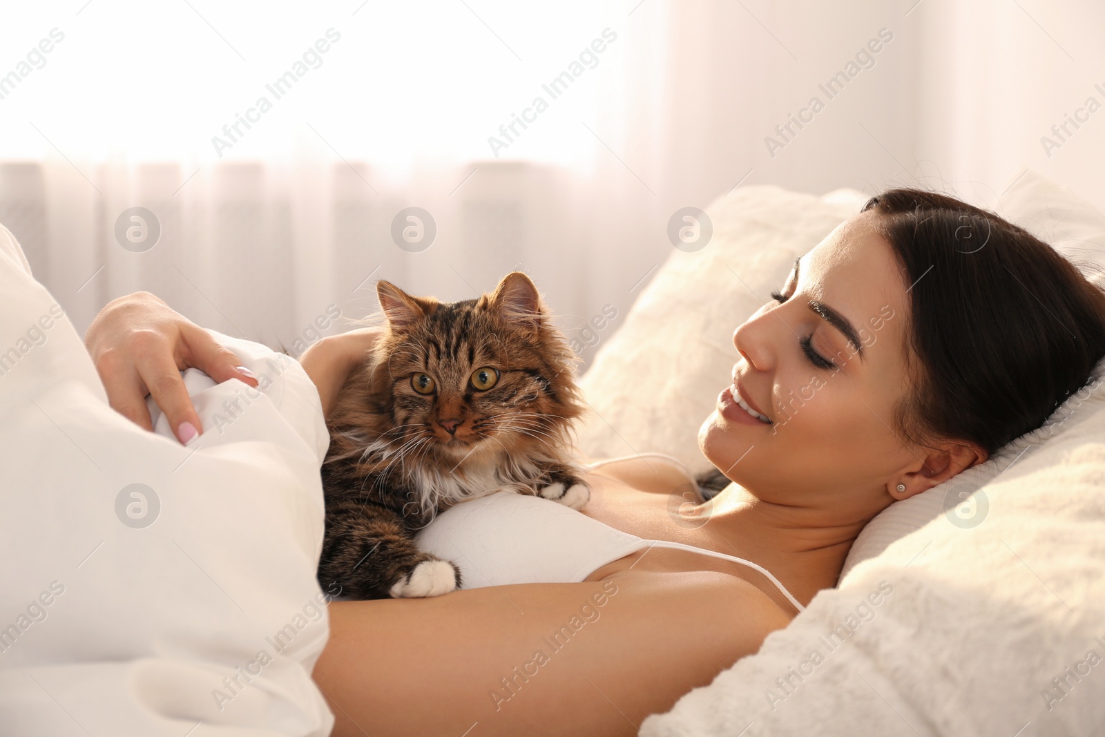 Photo of Beautiful young woman with her cute cat on bed. Fluffy pet