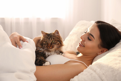 Photo of Beautiful young woman with her cute cat on bed. Fluffy pet