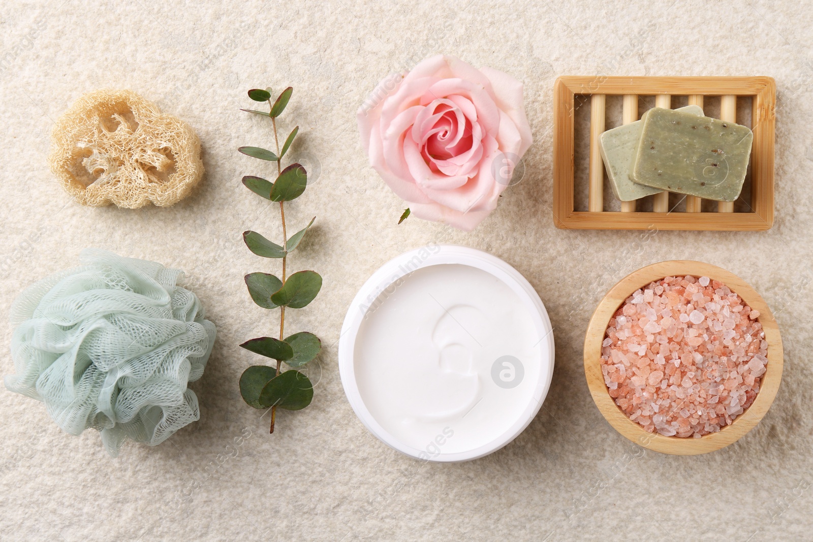 Photo of Flat lay composition with moisturizing cream in open jar and other body care products on light textured table