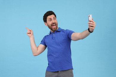 Photo of Happy man taking selfie with smartphone on light blue background