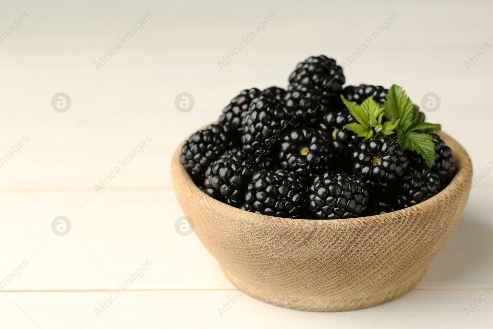 Photo of Bowl with fresh ripe blackberries on white wooden table, closeup. Space for text