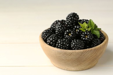 Photo of Bowl with fresh ripe blackberries on white wooden table, closeup. Space for text