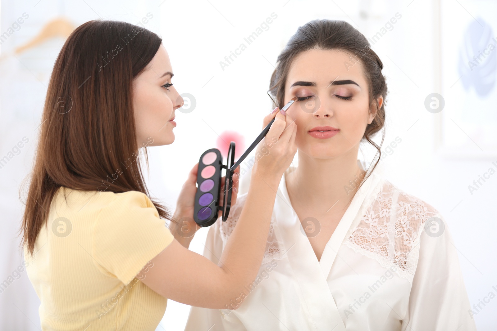 Photo of Professional makeup artist working with young woman in salon