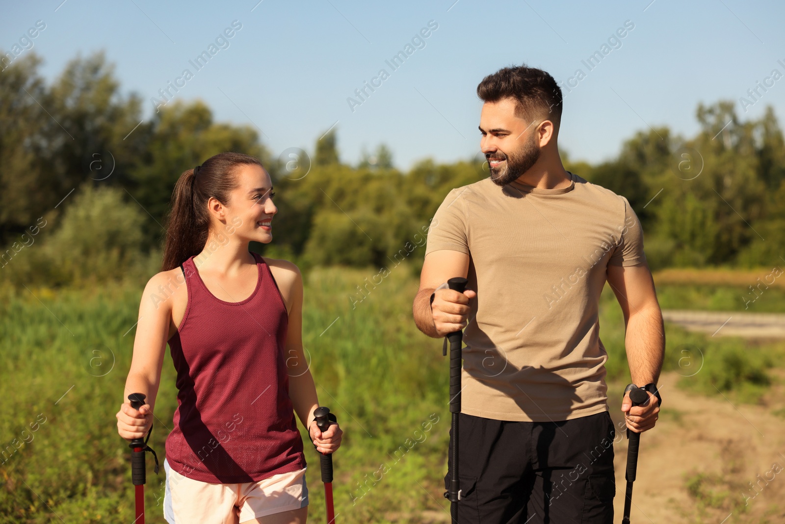 Photo of Happy couple practicing Nordic walking with poles outdoors on sunny day