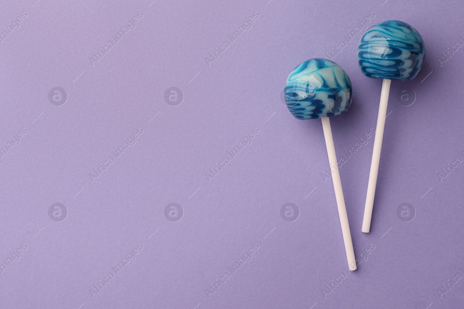 Photo of Tasty lollipops on violet background, flat lay. Space for text