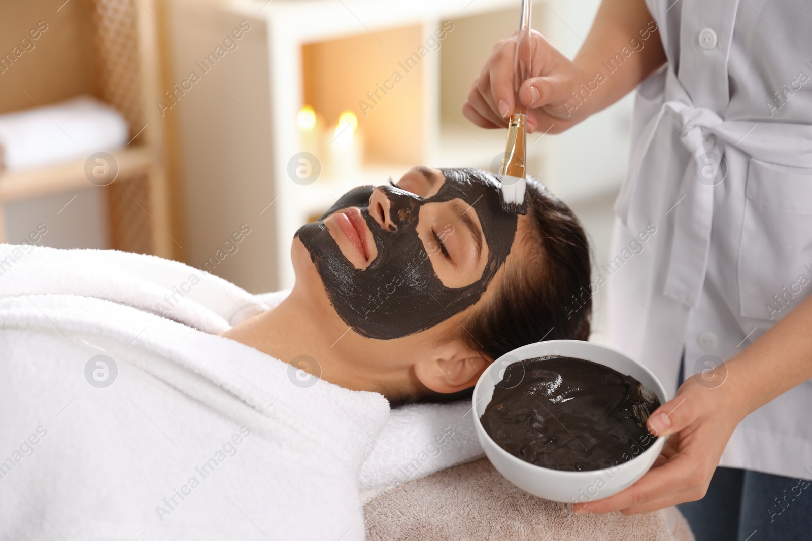 Photo of Cosmetologist applying black mask onto woman's face in spa salon