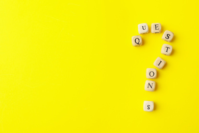 Photo of Wooden cubes with word QUESTIONS on yellow background, flat lay. Space for text