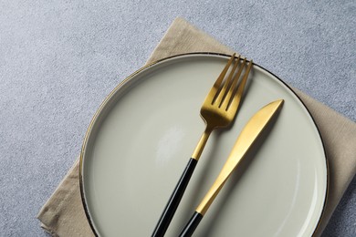 Photo of Stylish golden cutlery, plate and napkin on grey table, top view