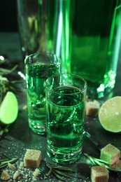 Absinthe in shot glasses, brown sugar, lime and rosemary on gray table, closeup. Alcoholic drink