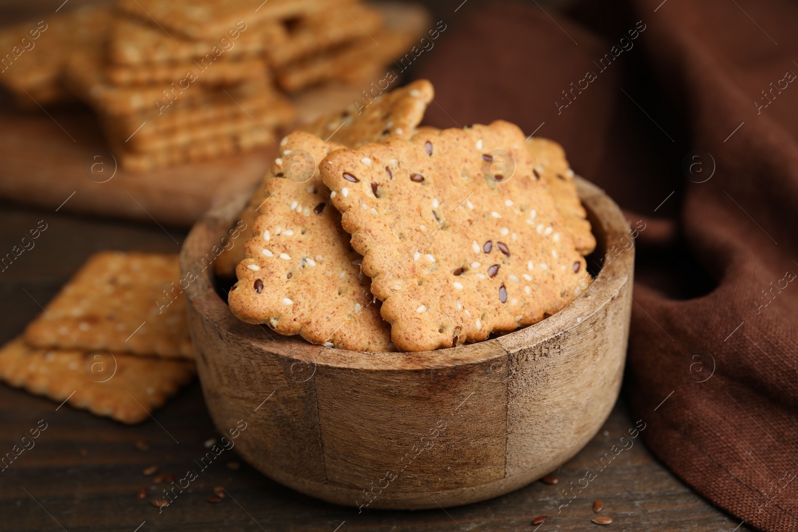 Photo of Cereal crackers with flax and sesame seeds in bowl on wooden table, closeup