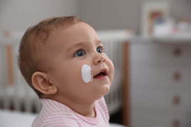 Photo of Cute little baby with moisturizing cream on her face at home, closeup. Space for text