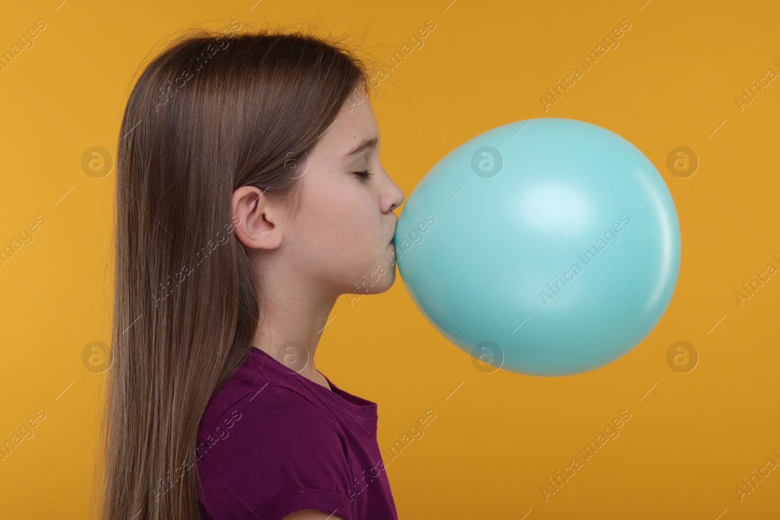 Photo of Girl inflating bright balloon on orange background