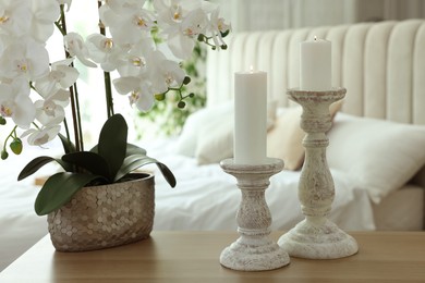 Photo of Pair of beautiful candlesticks and orchid plant on wooden table in bedroom