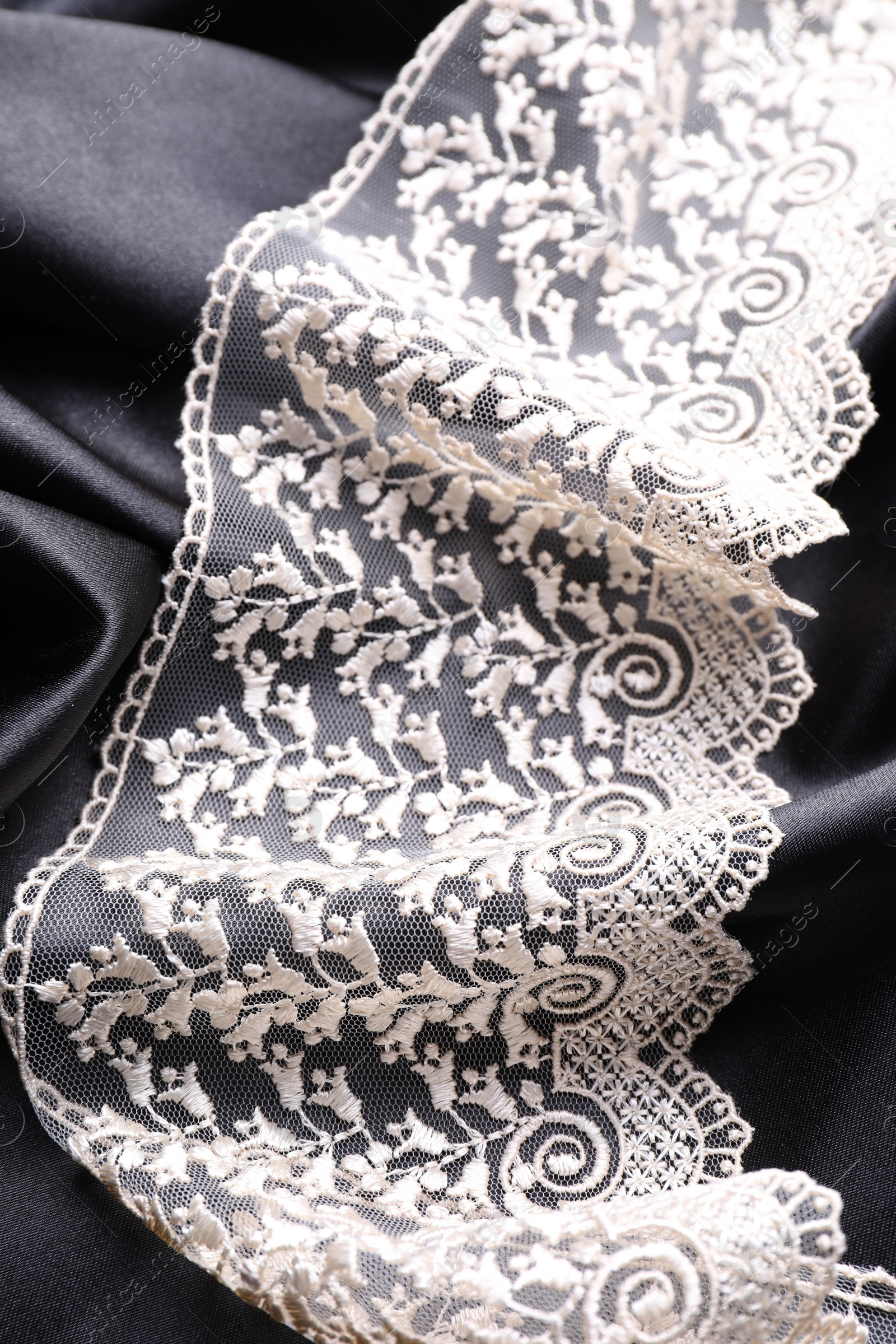 Photo of Beautiful white lace on black fabric, top view