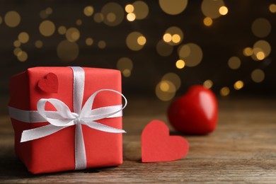 Photo of Beautiful gift box with red hearts on wooden table against blurred lights, closeup
