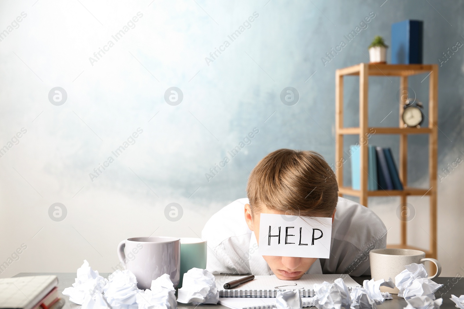 Photo of Young man with note HELP on forehead at workplace. Space for text