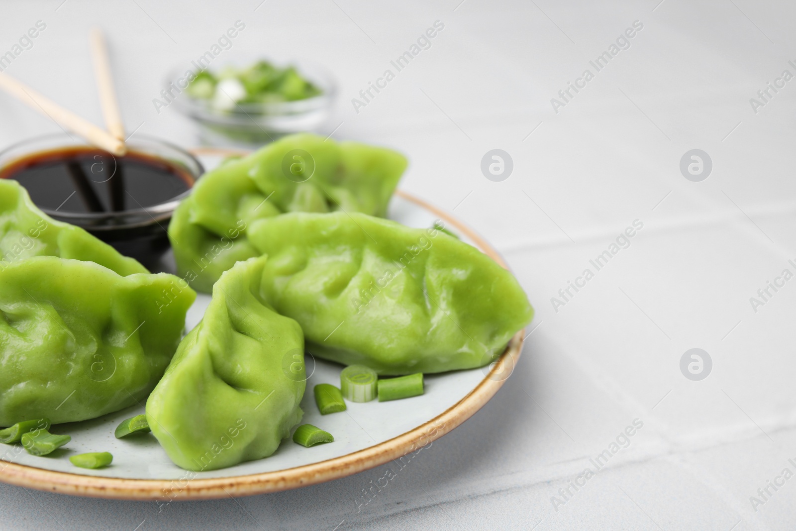 Photo of Delicious green dumplings (gyozas) and soy sauce on white tiled table, closeup. Space for text