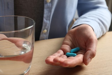 Photo of Woman with glass of water and pills at wooden table, closeup