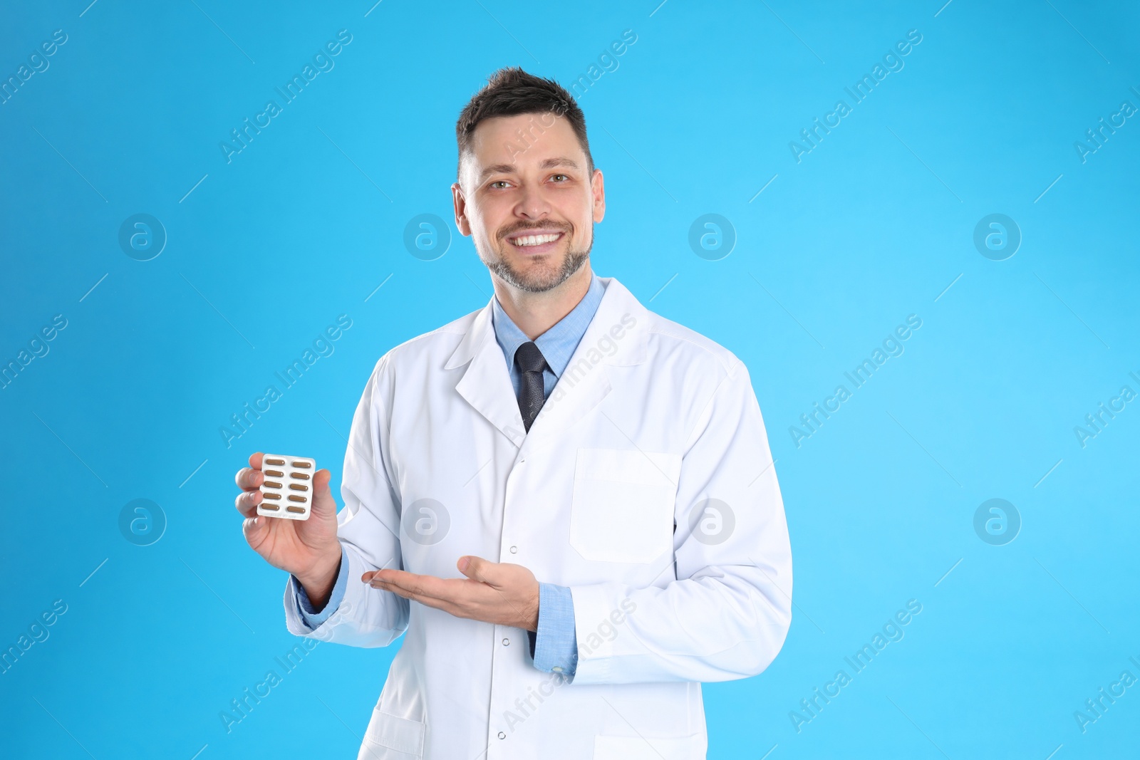 Photo of Professional pharmacist with pills on light blue background