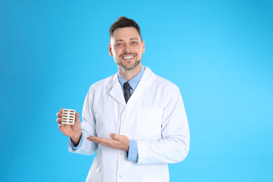 Professional pharmacist with pills on light blue background