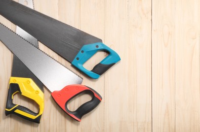 Photo of Saws with colorful handles on wooden background, flat lay. Space for text