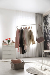 Photo of Rack with stylish women's clothes and handbag indoors. Interior design