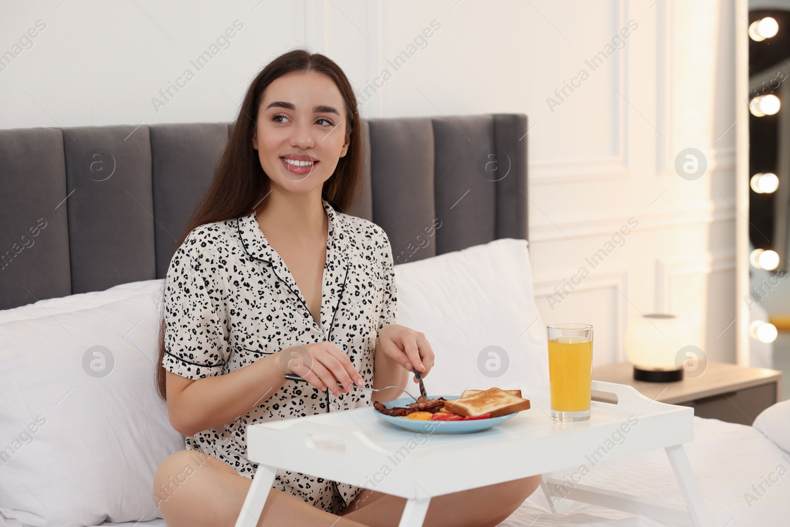 Photo of Happy young woman having breakfast on bed at home