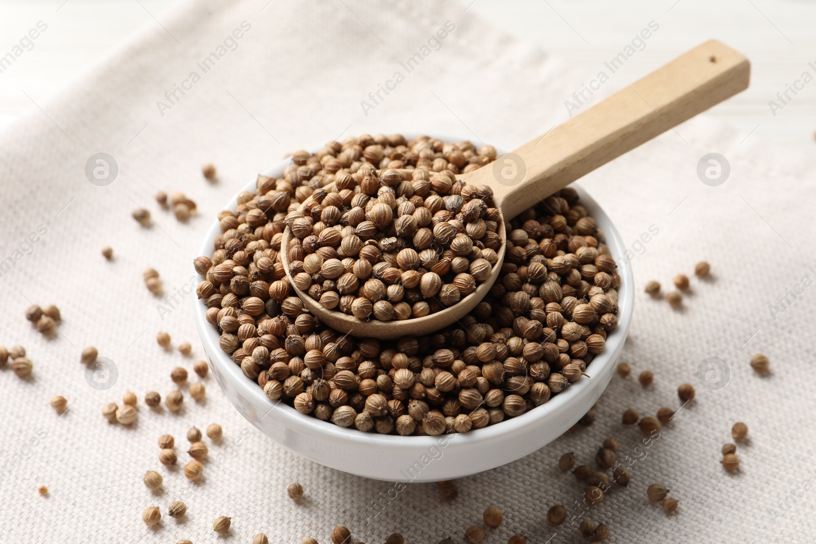 Photo of Dried coriander seeds in bowl and spoon on light cloth , closeup