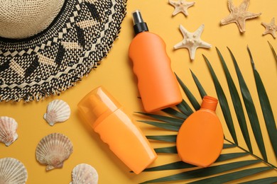 Sun protection products, shells and beach hat on orange background, flat lay