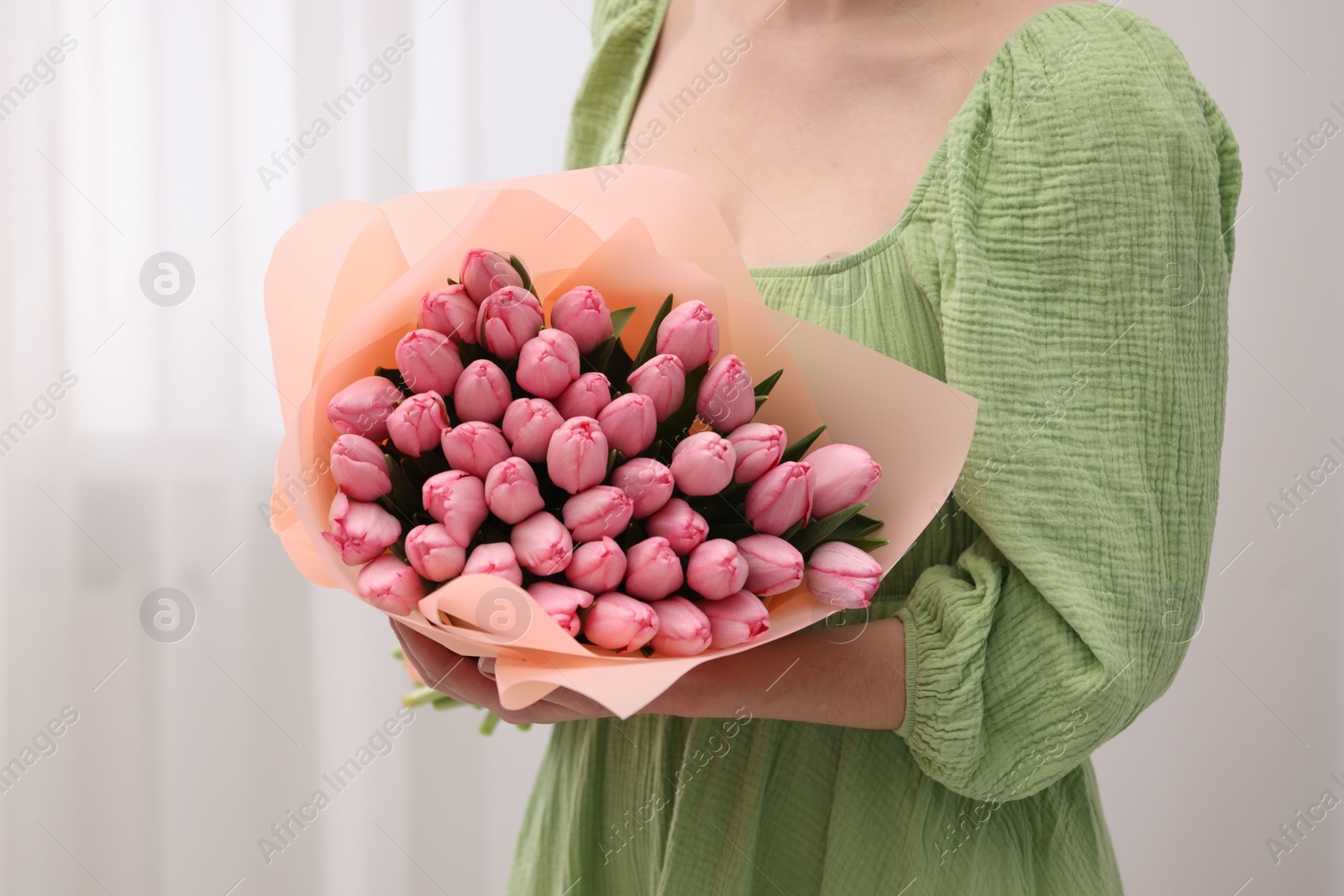 Photo of Woman holding bouquet of pink tulips indoors, closeup