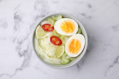 Photo of Bowl of delicious rice noodle soup with celery and egg on white marble table, top view
