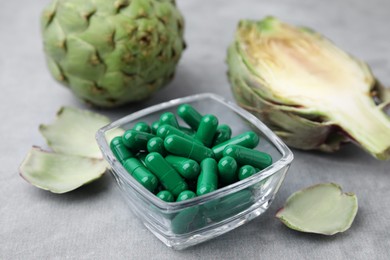 Photo of Bowl with pills and fresh artichokes on grey table, closeup