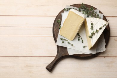 Photo of Board with pieces of tasty camembert cheese and thyme on light wooden table, top view. Space for text