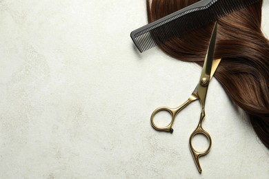 Photo of Professional hairdresser scissors and comb with brown hair strand on grey table, top view. Space for text