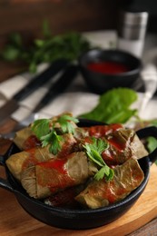 Photo of Delicious stuffed grape leaves with tomato sauce on wooden board