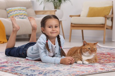 Photo of Smiling little girl and cute ginger cat on carpet at home