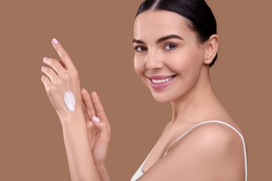 Photo of Beautiful woman with smear of body cream on her hand against light brown background